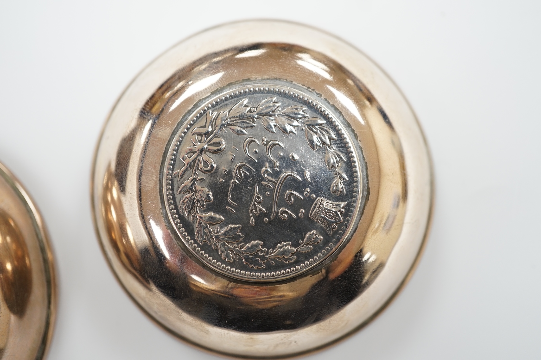 A Tibetan white metal mounted cup, two coin inset dishes and a silver matchbox holder, largest 11.5cm diameter